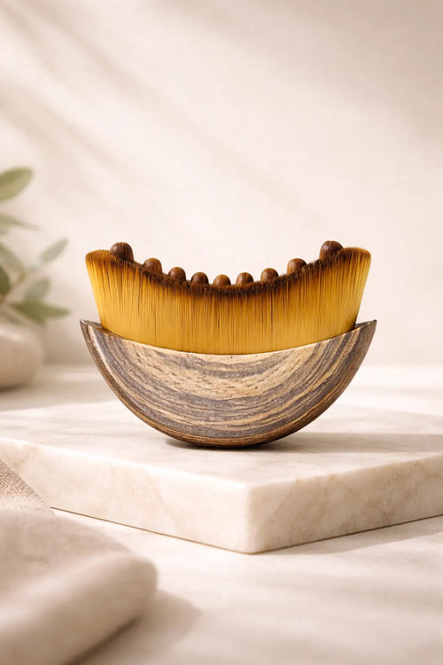 Cepillo de madera para drenaje linfático facial con cerdas sintéticas densas y nódulos de masaje sobre base de mármol.