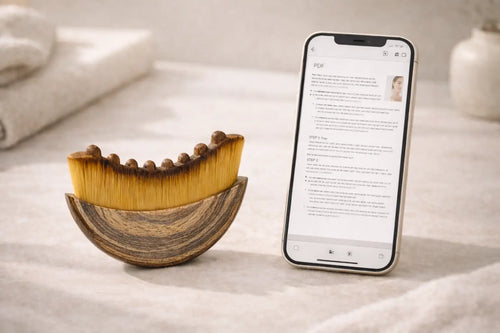 Cepillo de drenaje linfático facial junto a un smartphone que muestra una guía de uso en formato PDF sobre una superficie clara.
